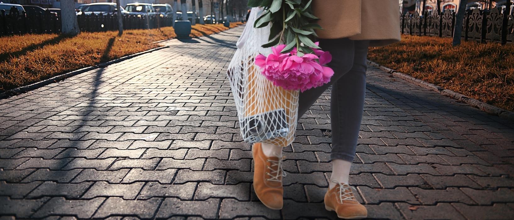 woman carrying reusable net bag with camera and other items in, as well as a bouquet of flowers