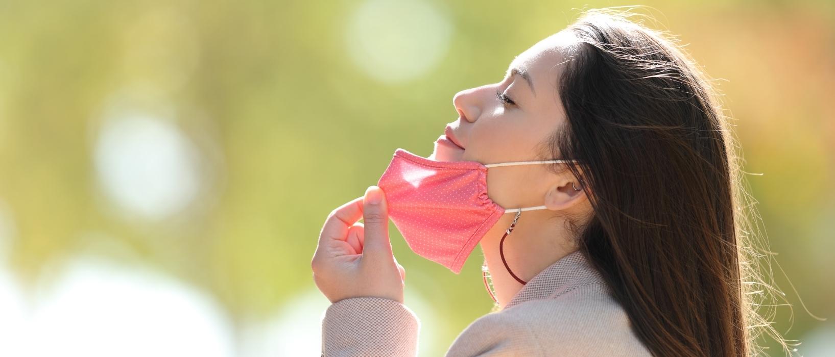 side portrait of woman removing face mask and smiling while breathing in outside air