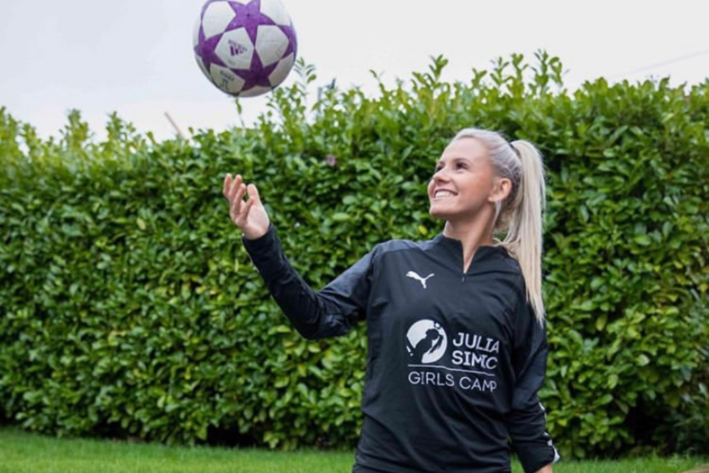 Julia Simic throwing football in air, wearing black shirt with Julia Simic Girls Camp written on it