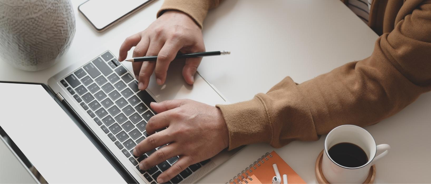 close up of hands typing on laptop, mug of coffee nearby